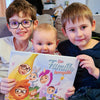 Trois enfants, dont un bébé, avec leur livre personnalisé pour les familles livré avec sa pochette.